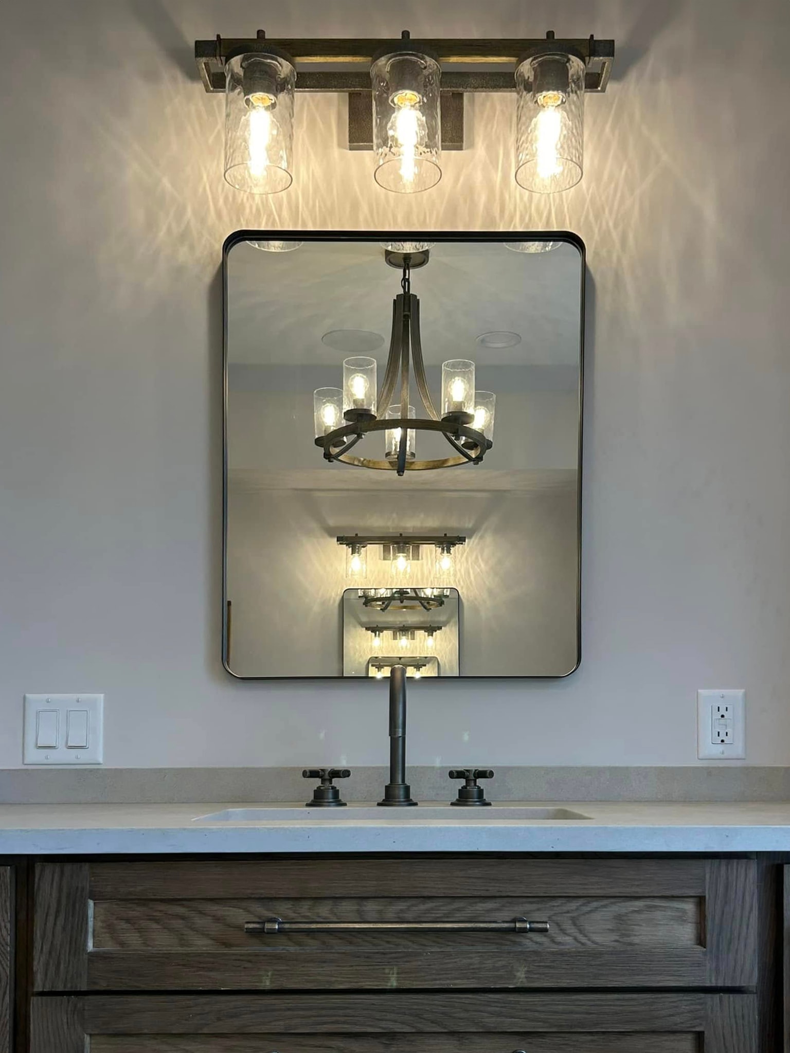 Vanity with industrial-style lighting, square mirror and dark wood cabinetry