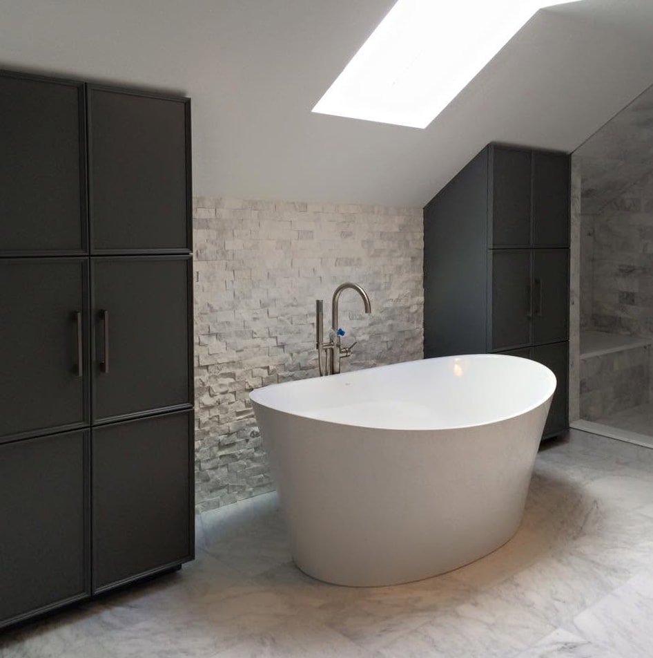 Minimalist bathroom with freestanding soaker tub, stone accent wall and skylight