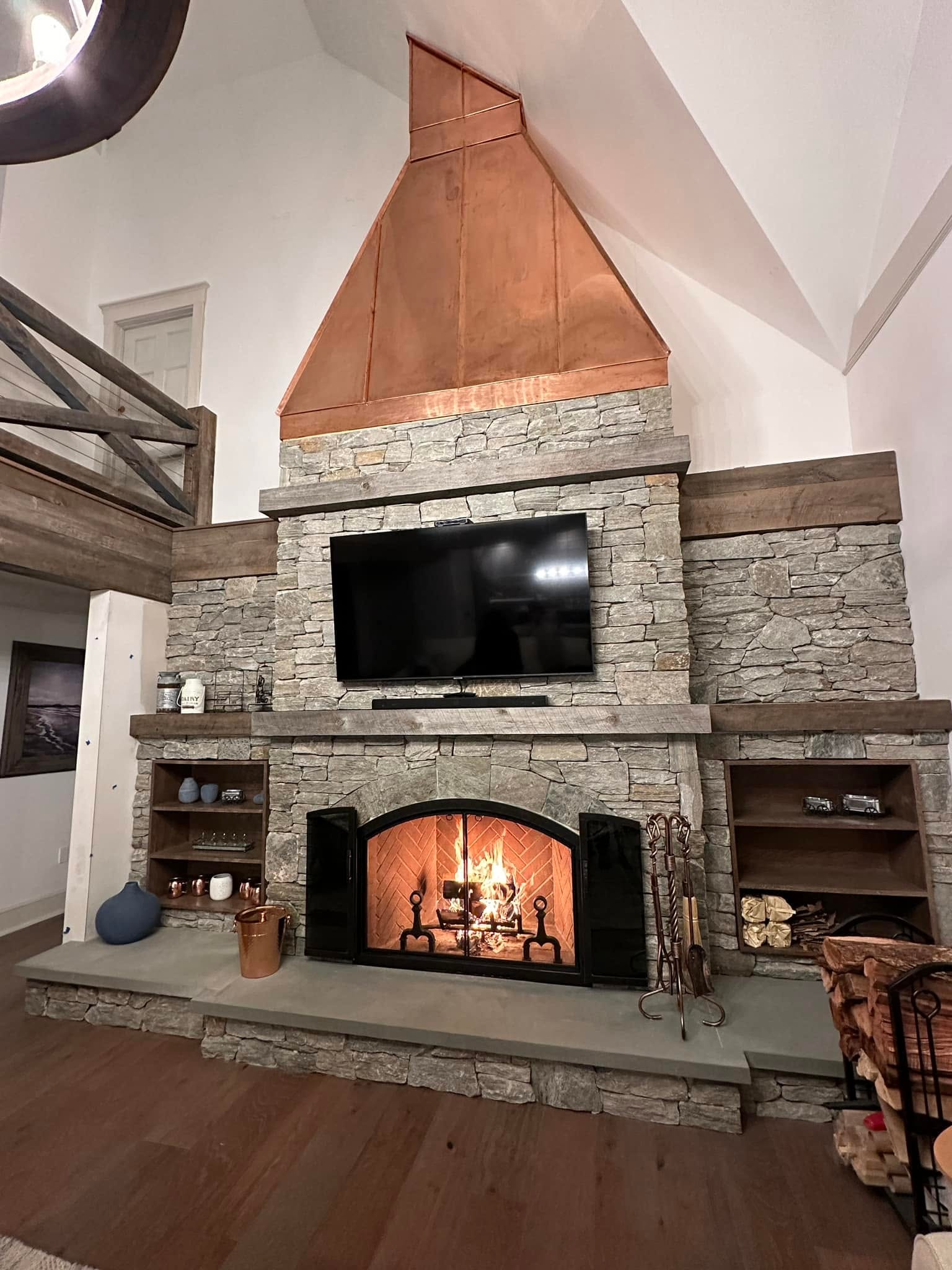 Stone fireplace with copper hood, built-in shelving and vaulted ceiling