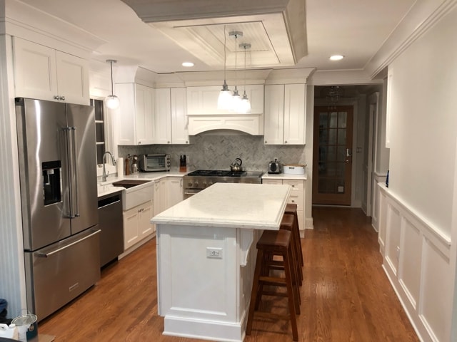 White kitchen with island, herringbone tile backsplash and stainless appliances